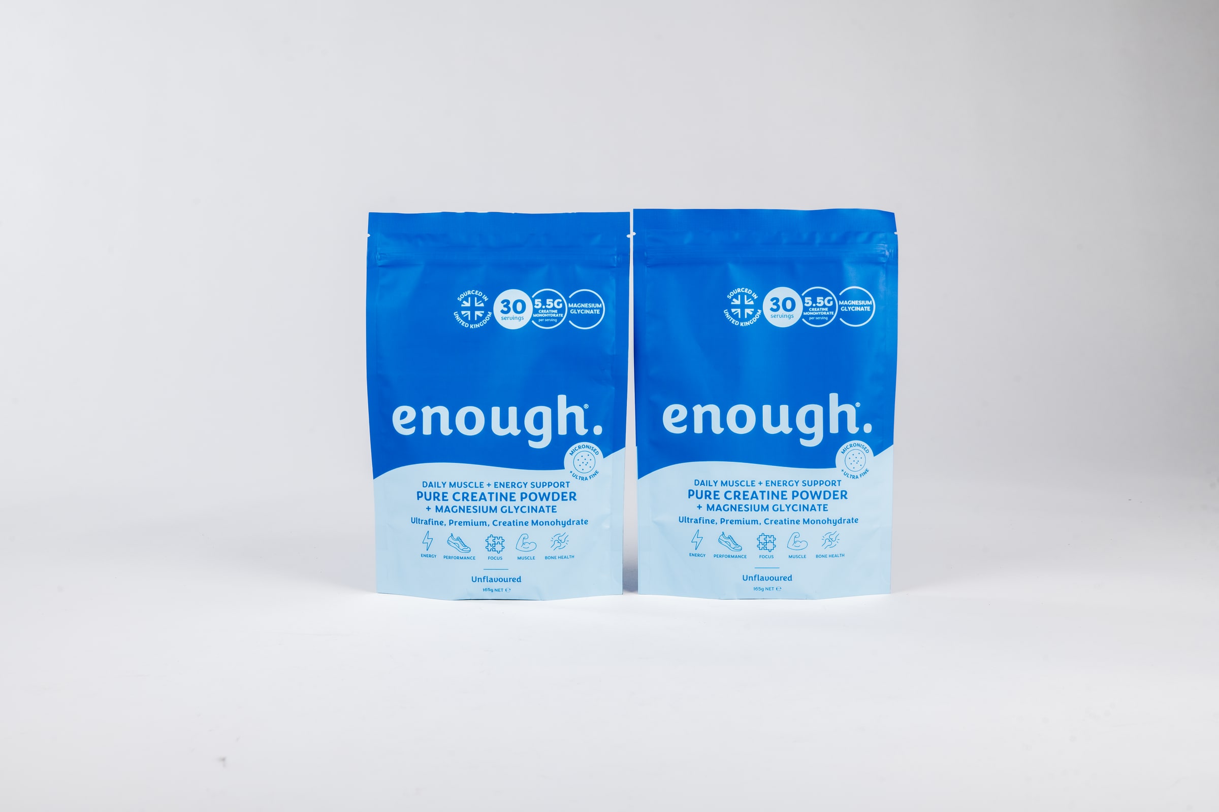 Two blue Enough Wellness creatine powder pouches standing side by side in the middle of a seamless white studio backdrop