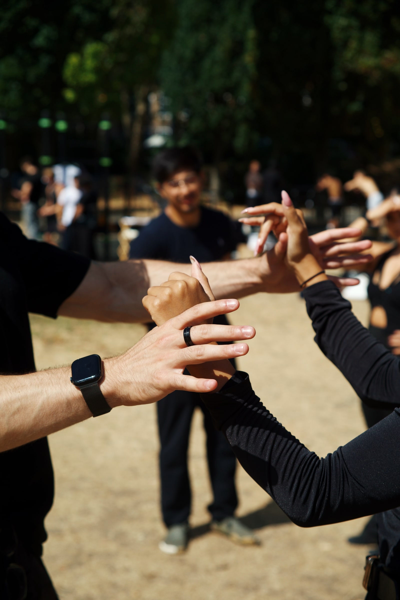 Close-up of dancers' raised hands meeting mid-move at an outdoor bachata session, a smiling man blurred in the sunlit background