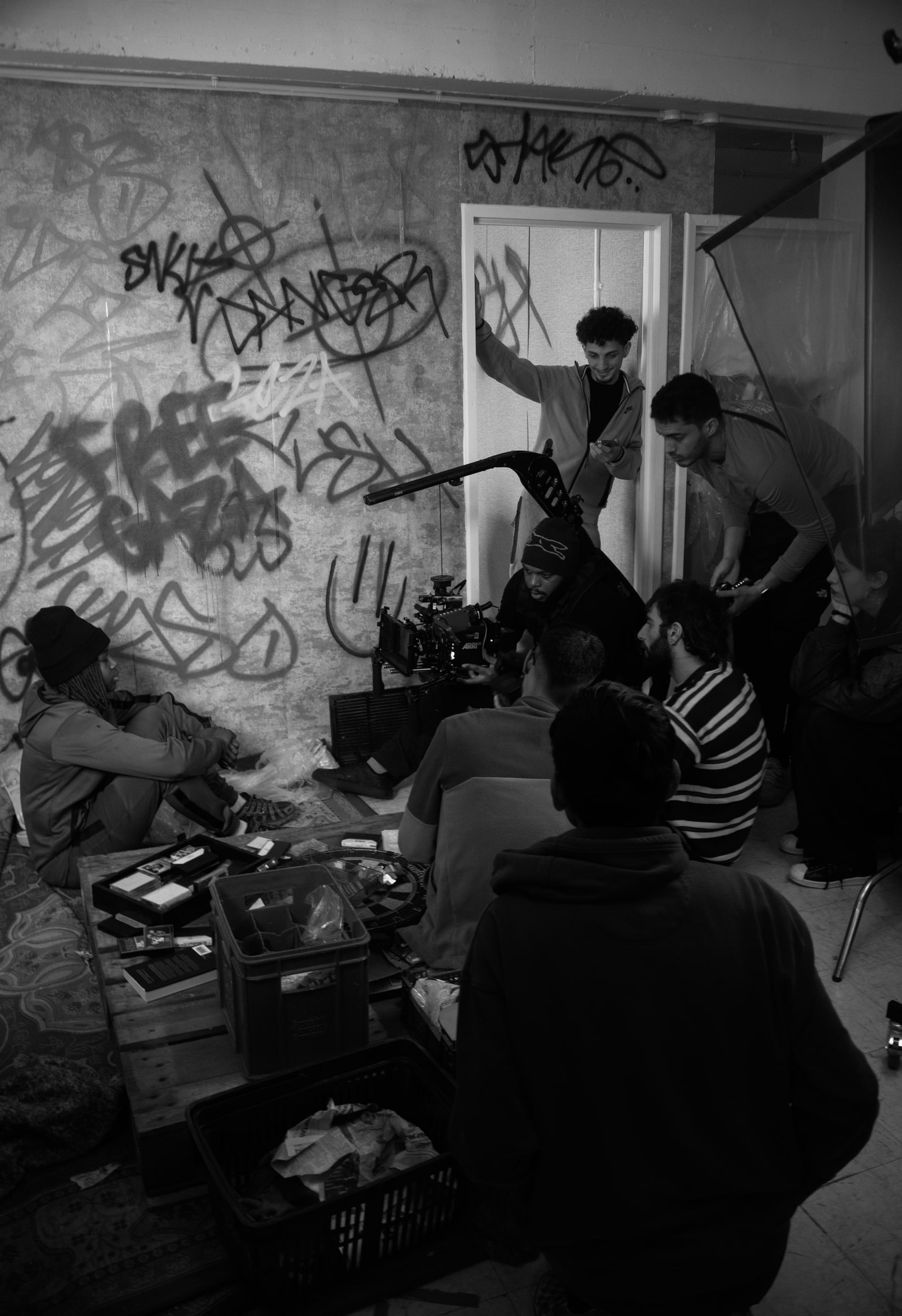 Cast and crew squeeze into a graffiti-covered room set around a camera on a rig, an actor in a hoodie crouched against the wall
